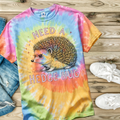 Colorful tie-dye t-shirt with a hedgehog graphic and text on a wooden surface.