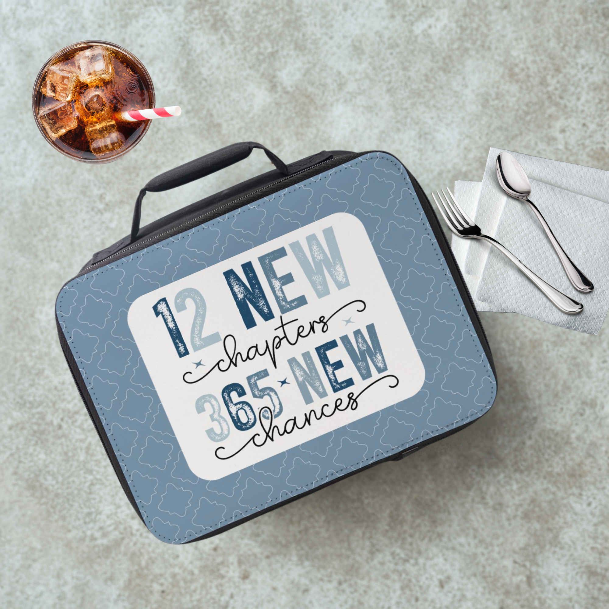 Lunch box with motivational quote on a cafeteria table with a drink and utensils.