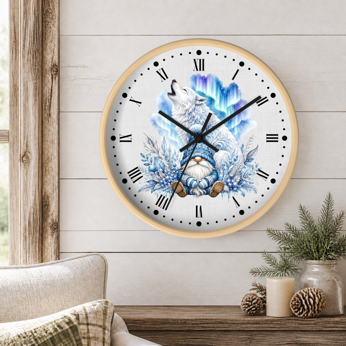 A round wall clock with a light wood frame hangs on a white shiplap wall above a wooden table with pinecones and a small plant. The clock face features a winter illustration of a white wolf howling at a glowing blue aurora borealis, surrounded by snowflakes and a small gnome.