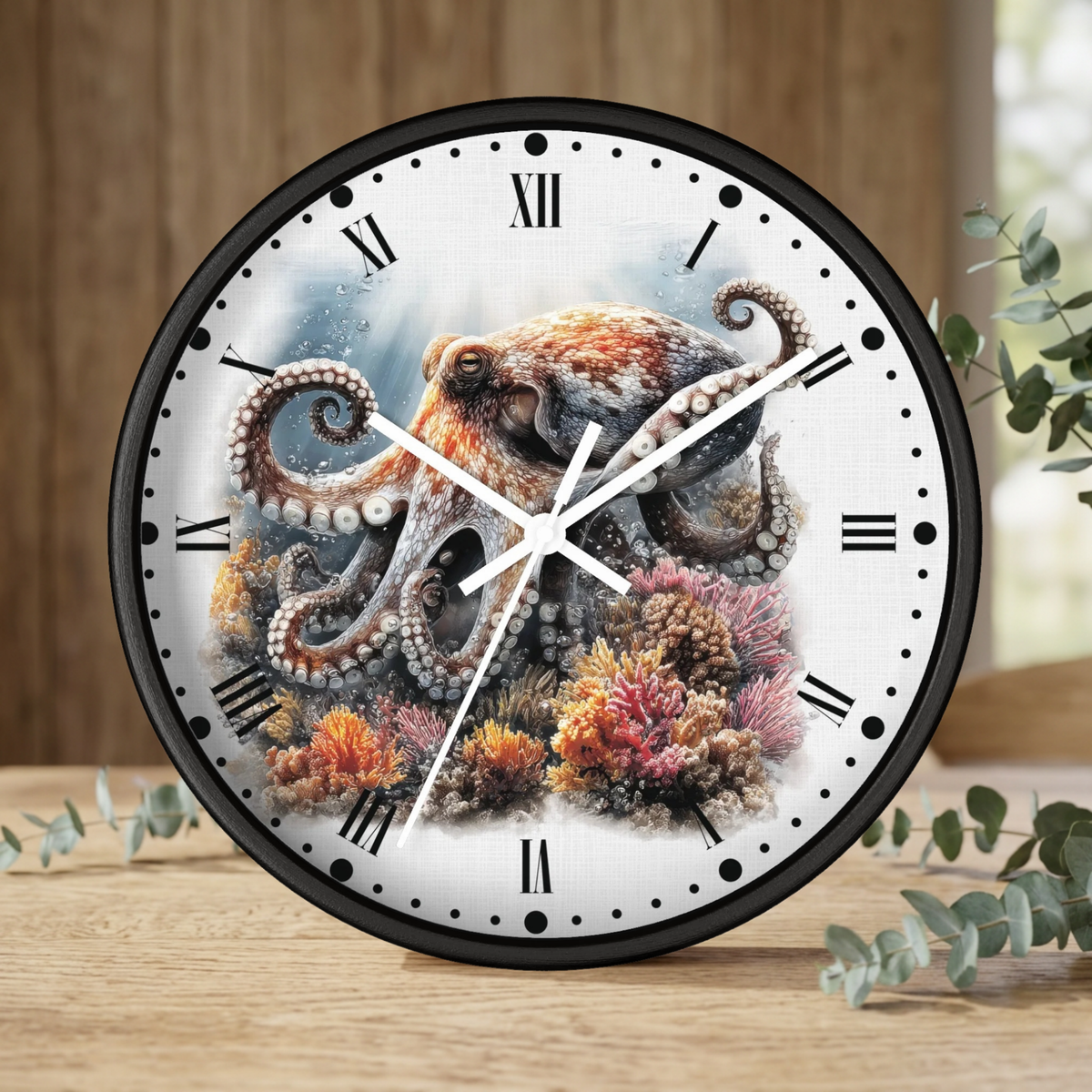 A round wall clock with a black frame and a white face featuring a detailed illustration of an octopus among colorful coral reef motifs. The clock is styled on a wooden tabletop with eucalyptus leaves and a wooden wall background.