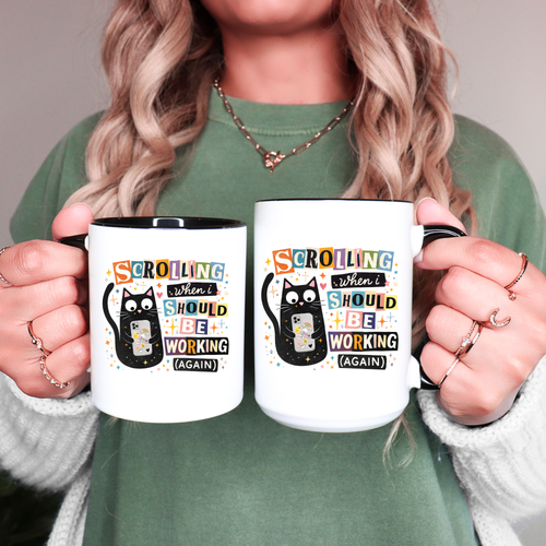 Person holding two mugs with a humorous cat design and text.