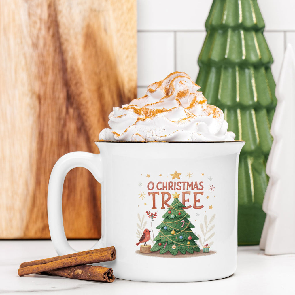 White mug with Christmas design featuring a tree and text, filled with hot chocolate and whipped cream, on a wooden surface.