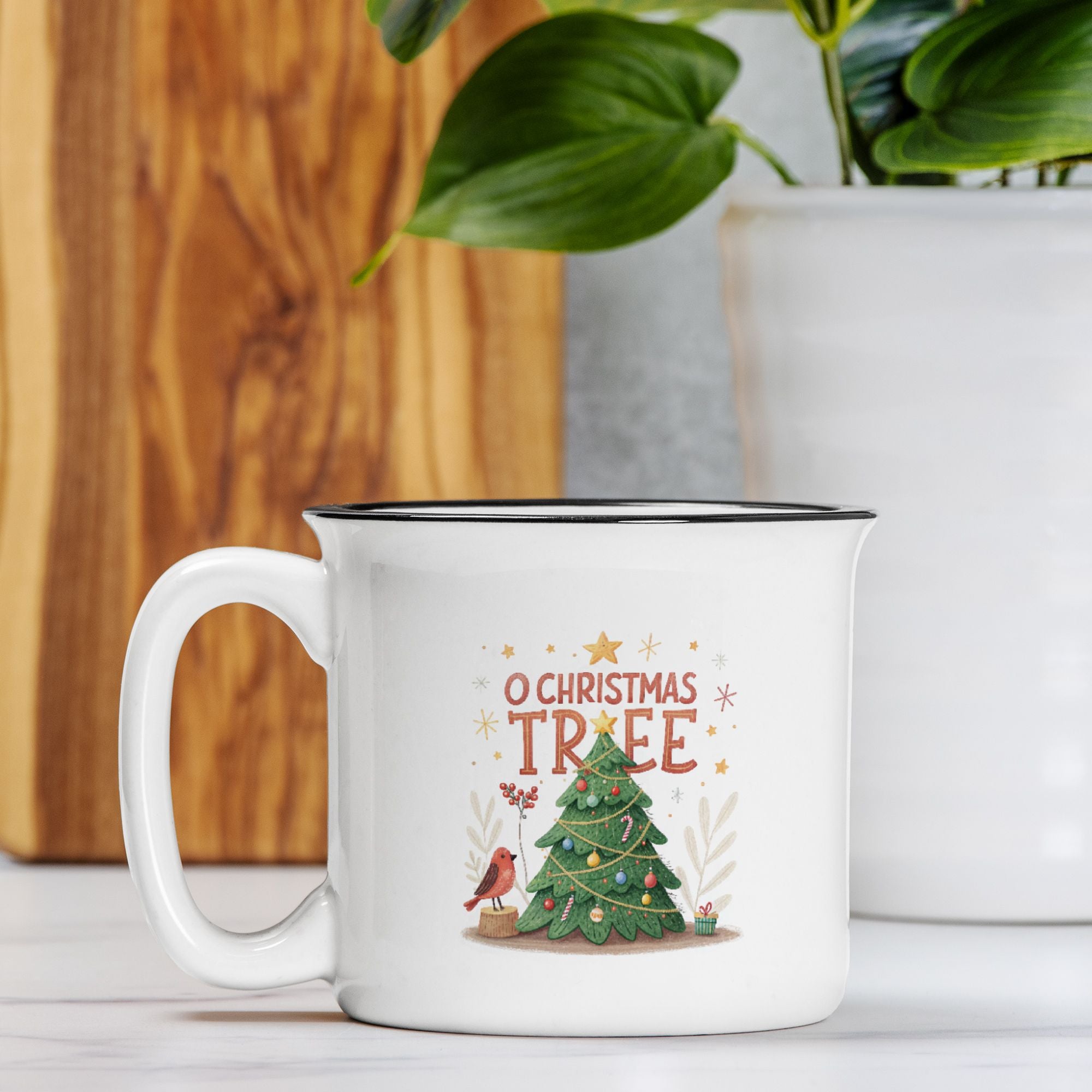 White mug with Christmas design featuring a tree and text, placed on a surface with a plant in the background.