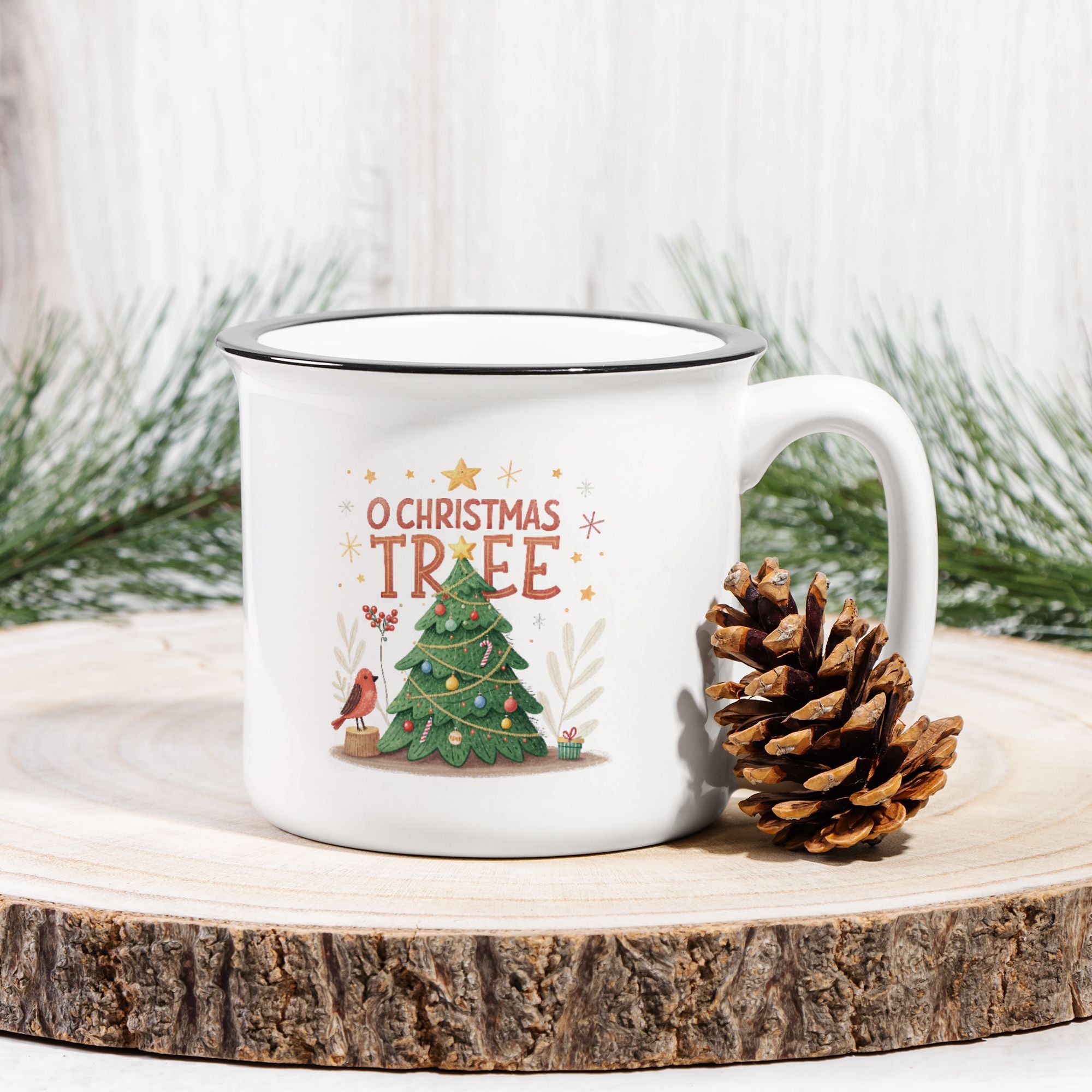 White mug with Christmas design featuring a tree and text, placed on a wooden surface with a pine cone and evergreen branches.