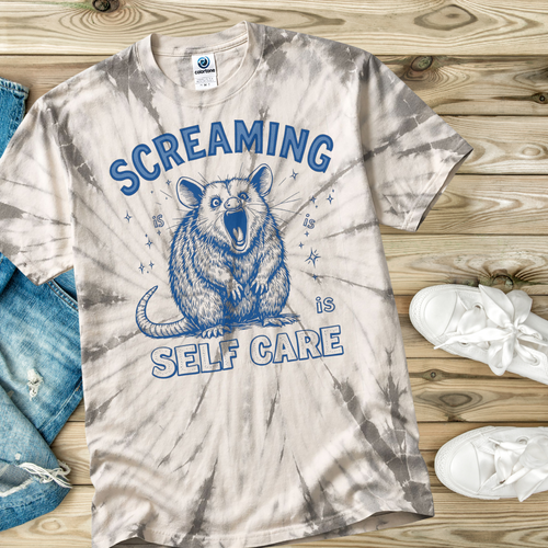 Tie-dye t-shirt with a graphic of an opossum and text 'Screaming is Self Care' on a wooden surface.