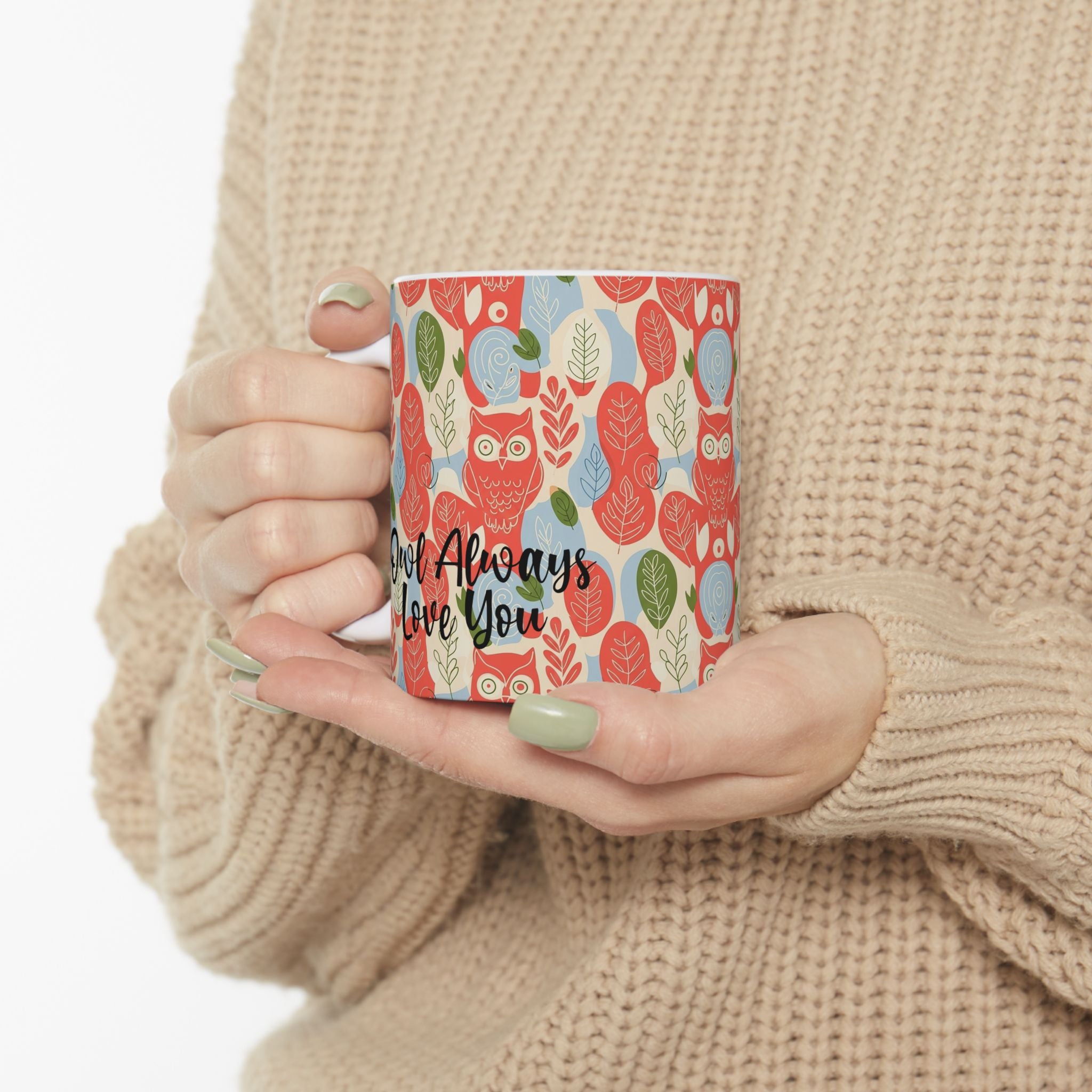 Person holding a mug with a colorful design and text, wearing a beige sweater.