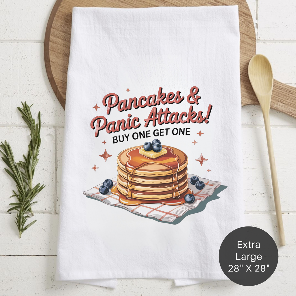 Tea towel with pancakes and text 'Pancakes & Panic Attacks! Buy One Get One' on a wooden board with utensils