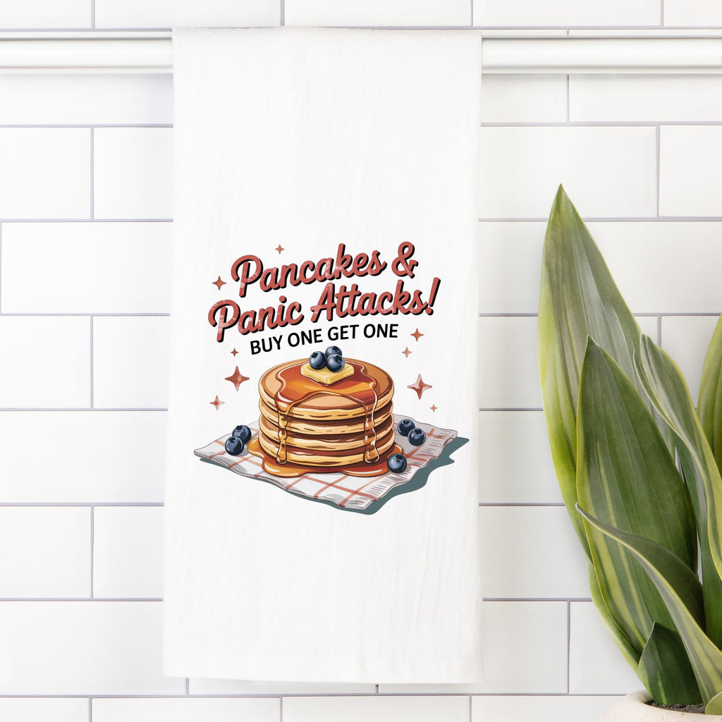 Tea towel with pancakes and text 'Pancakes & Panic Attacks! Buy One Get One' on a white tiled wall.