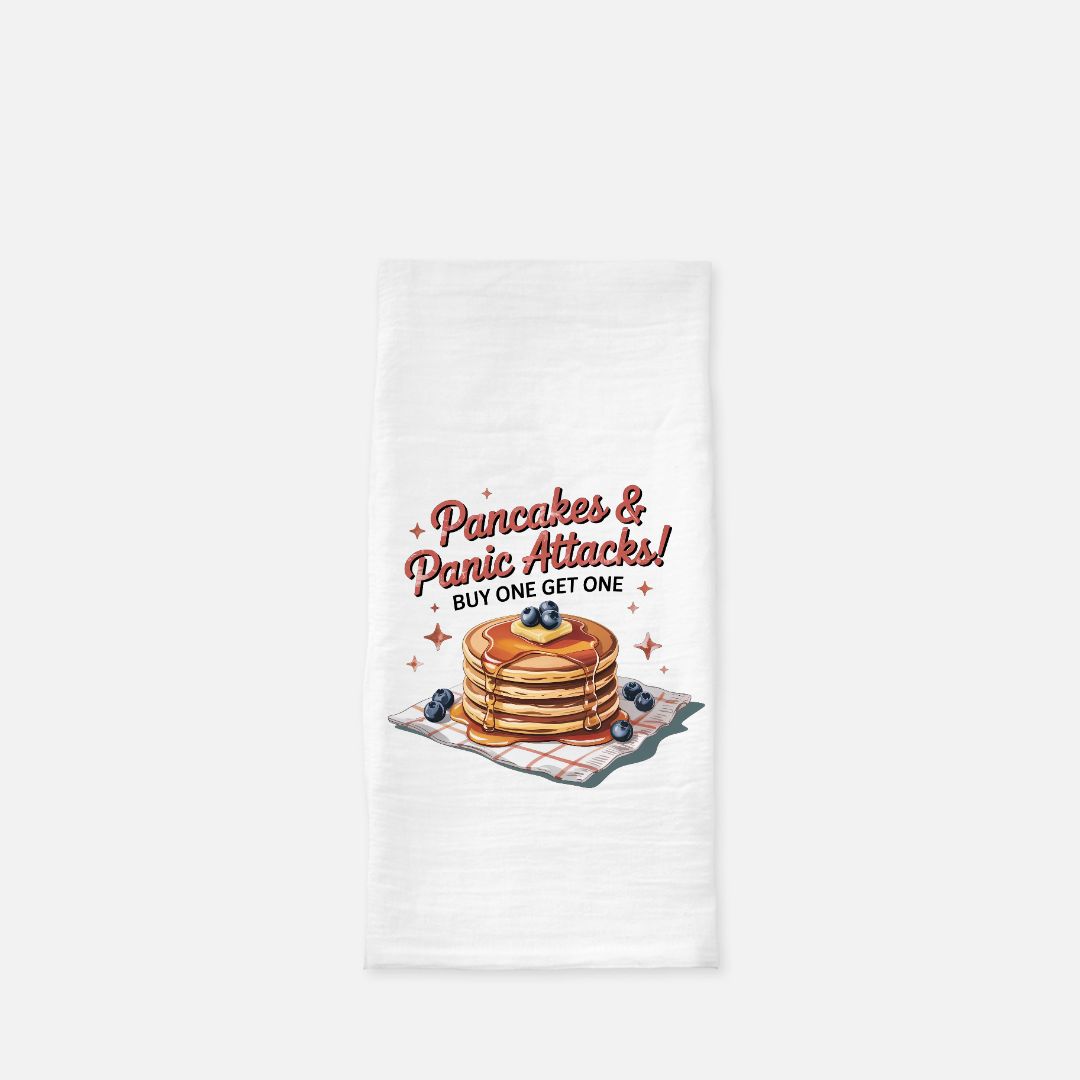 Tea towel with a design of pancakes and text 'Pancakes & Panic Attacks! Buy One Get One' on a white background.