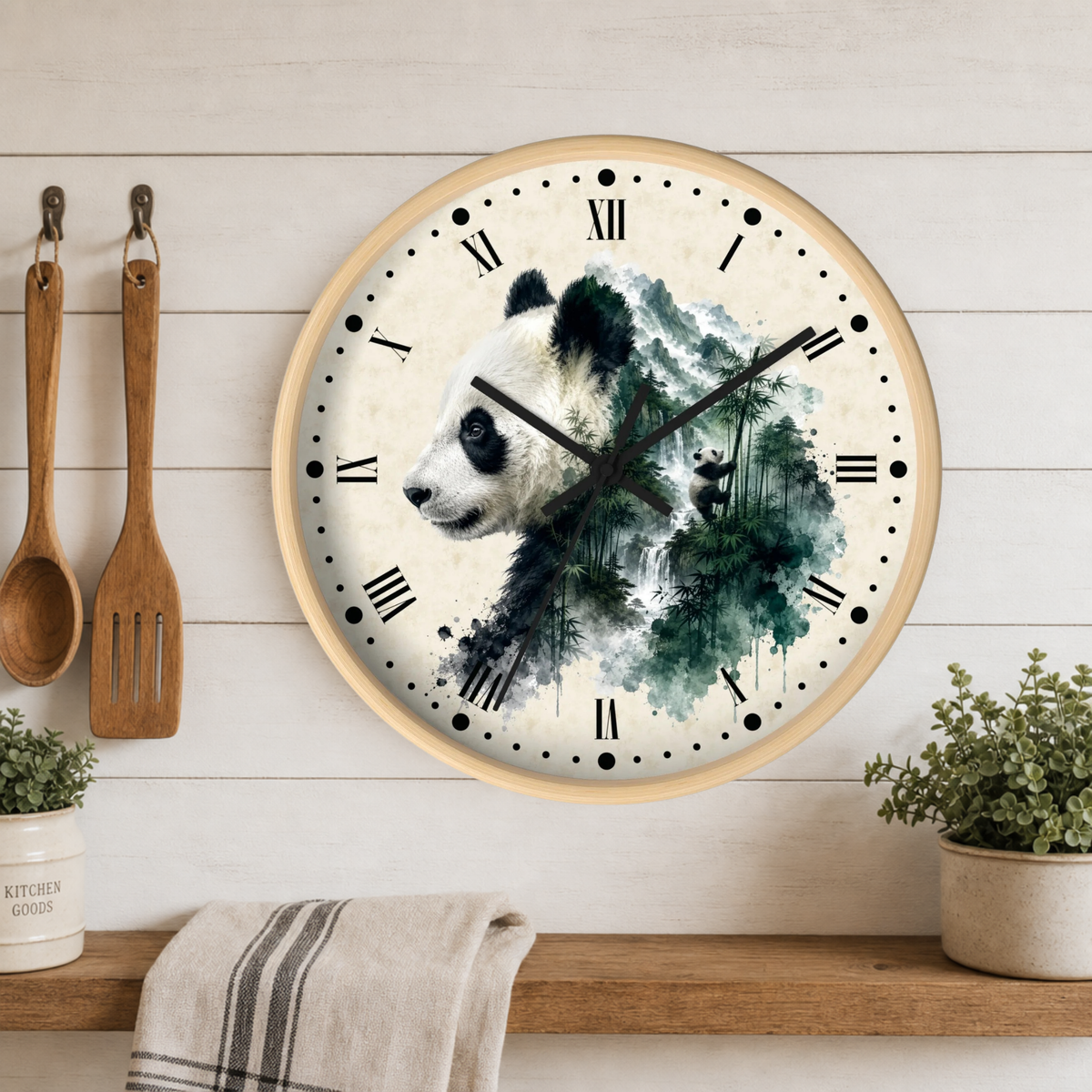 Round wall clock with a panda and forest watercolor design on the face, mounted on a white wood plank wall above a wooden shelf with kitchen utensils and plants.