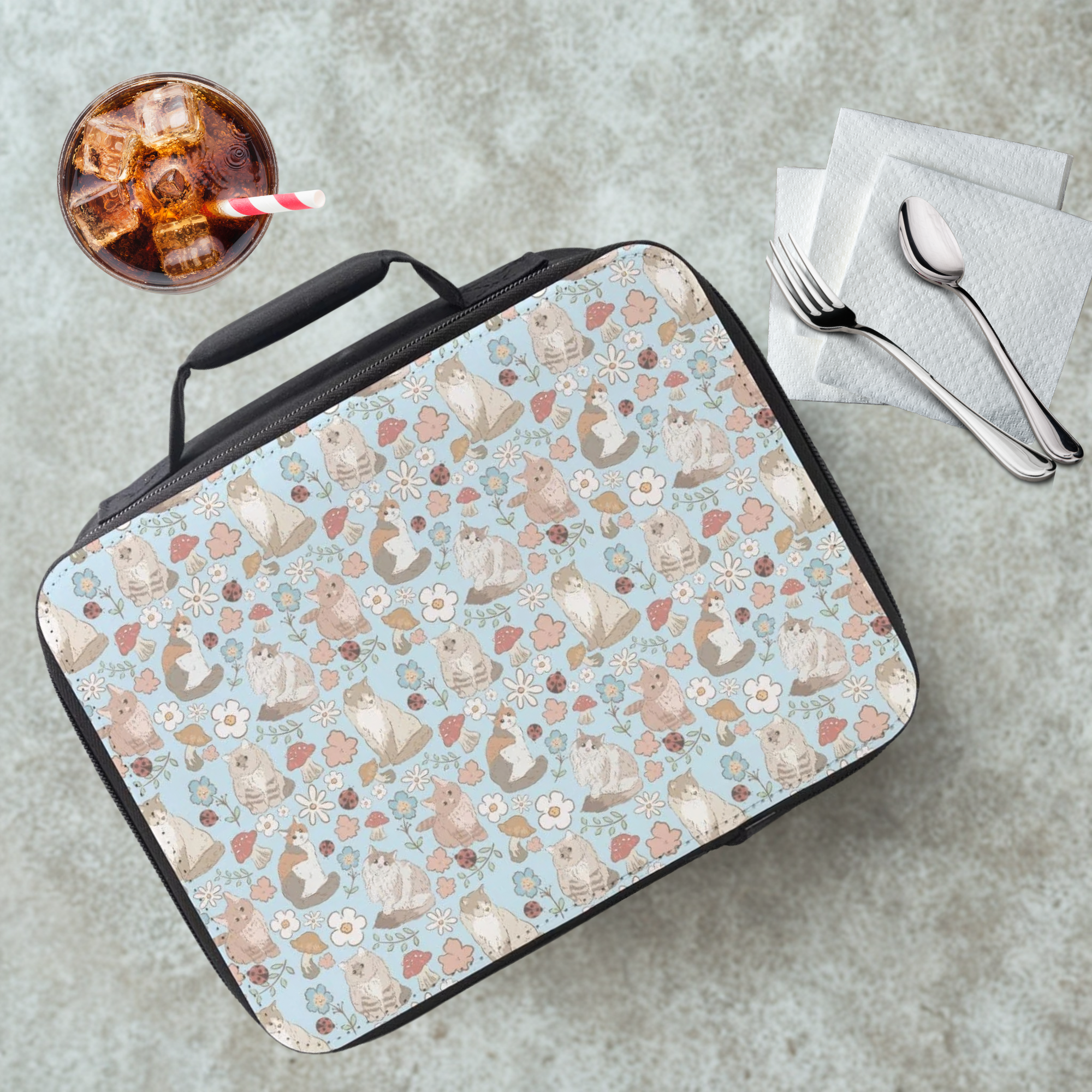 Lunch bag with a hand drawn cat pattern on a cafeteria table with a drink and utensils.