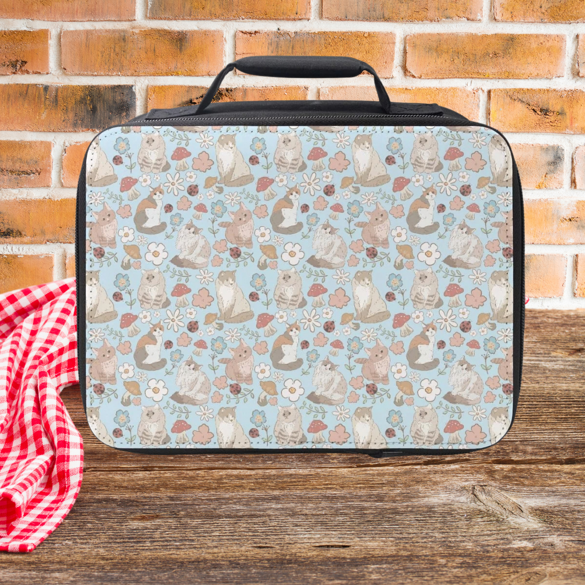 Lunch bag with hand drawn cat & flowers pattern on a wooden picnic table and brick wall background