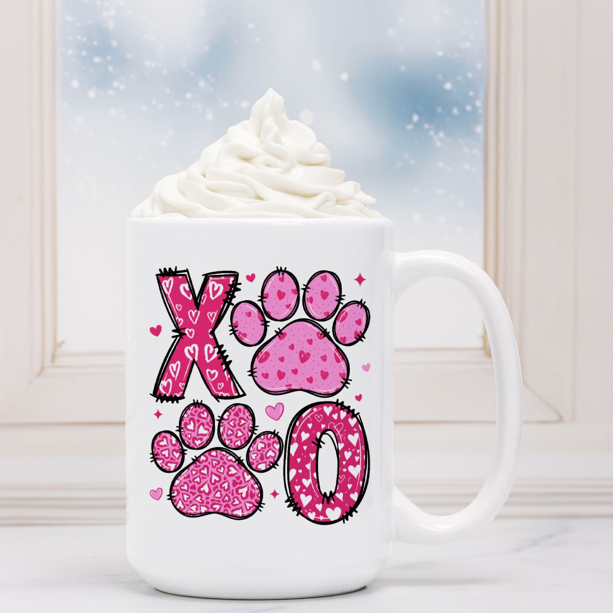 White mug with pink paw print design and heart details, filled with hot chocolate and whipped cream.