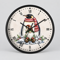 A round wall clock with a black frame and a festive Christmas penguin illustration on the dial. The clock face is off-white with black Roman numerals and black hands, while the penguin wears a red and white knit scarf and sits in a snowy winter scene with greenery.
