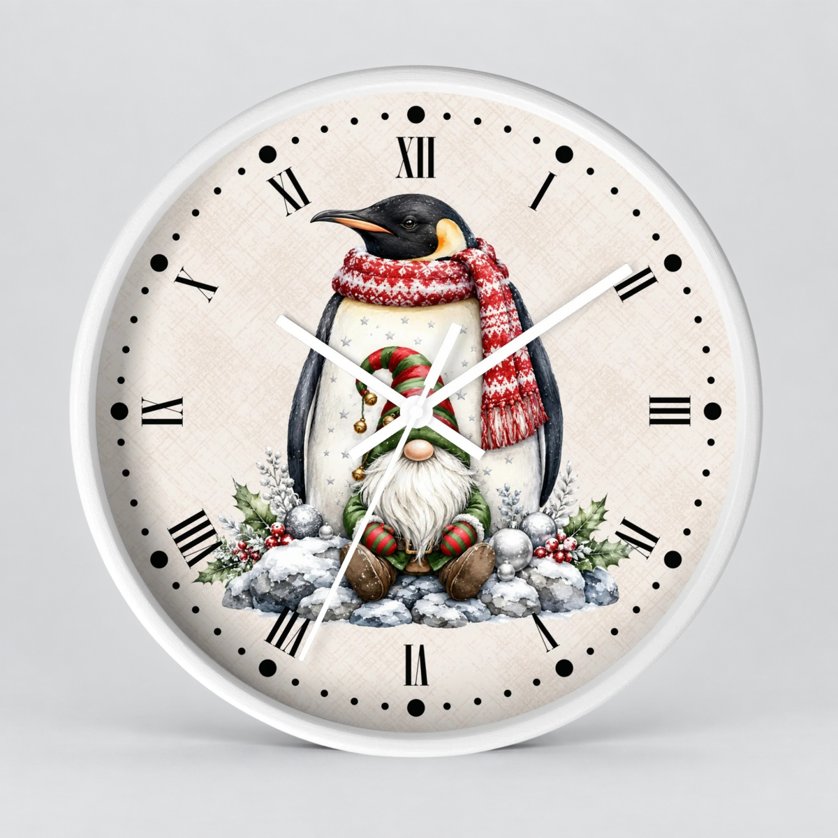 A round wall clock with a white frame and a cream-colored face, featuring a festive illustration of a penguin wearing a red knit scarf and a gnome sitting in the snow. The clock has black Roman numerals and black dot hour markers, with white clock hands.