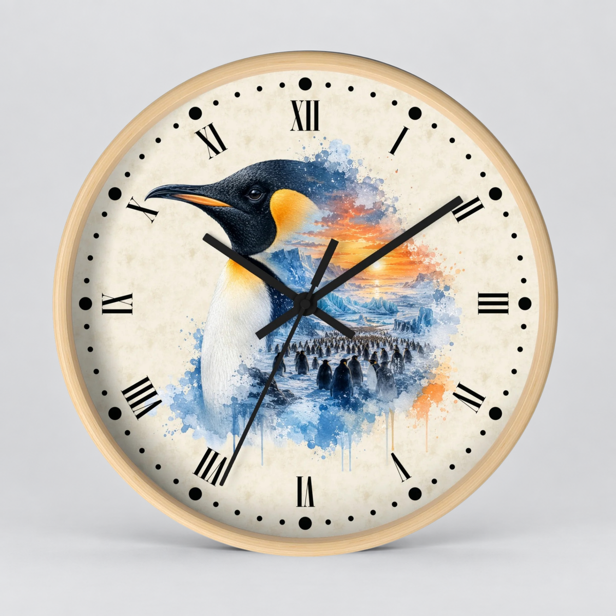 A round wall clock with a light wood frame and a cream-colored face featuring a watercolor-style penguin illustration in blue, black, white, and orange. The clock has black Roman numerals and black hands, photographed against a neutral light gray background.