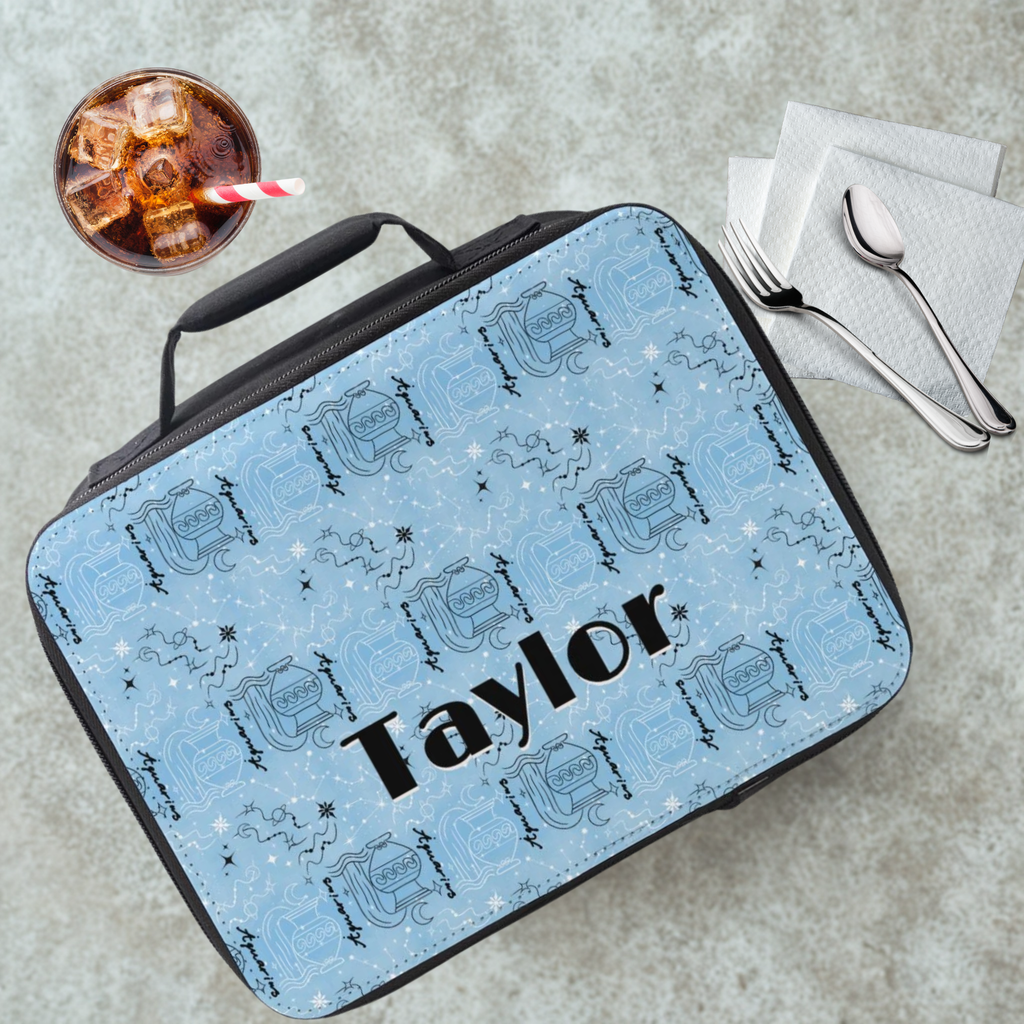 Blue and black Aquarius zodiac patterned lunch bag with 'Taylor' printed on it, placed on a cafeteria table with a drink and utensils in the background.