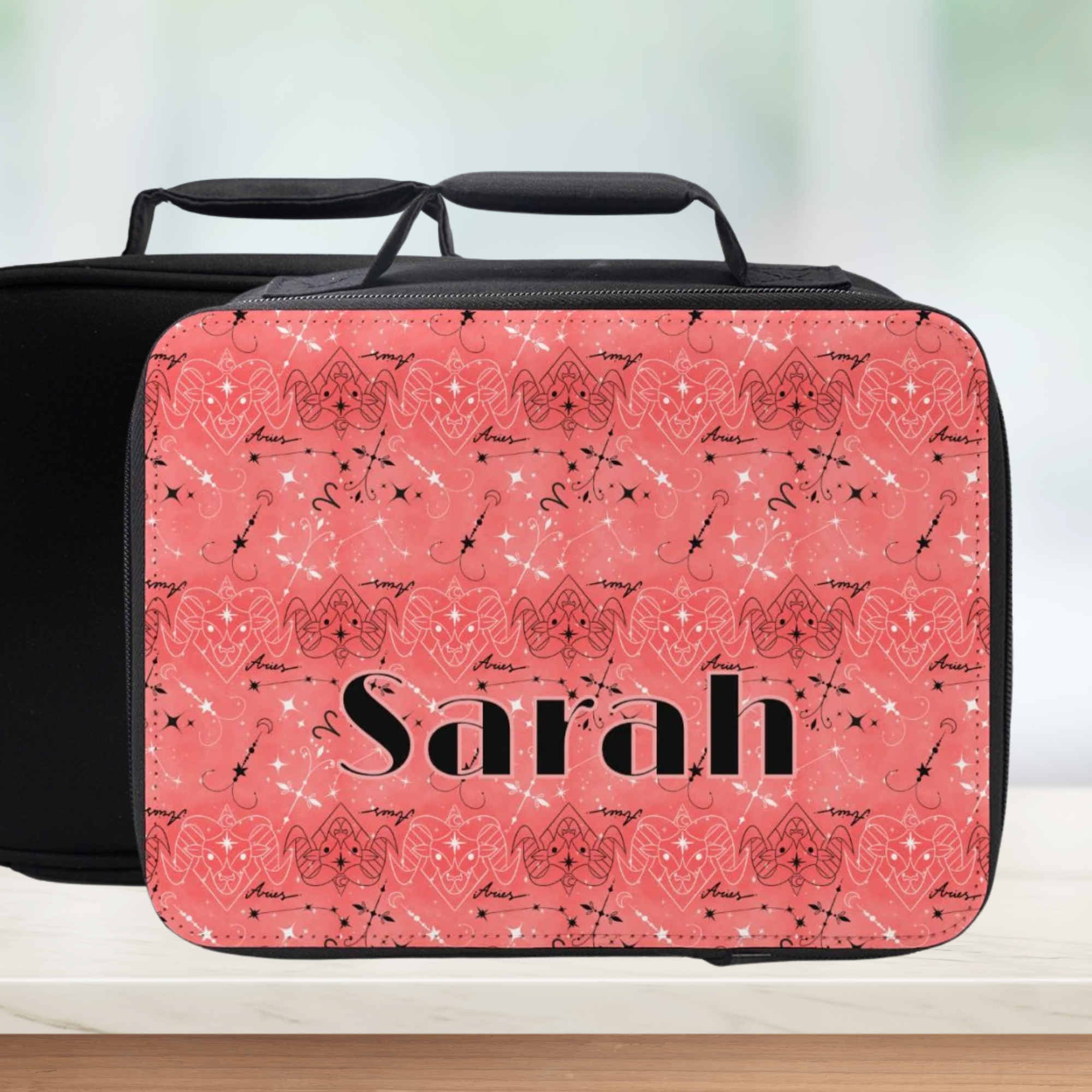 Pink and black lunch bag with Aries zodiac pattern and 'Sarah' custom text, on a counter with a light background.