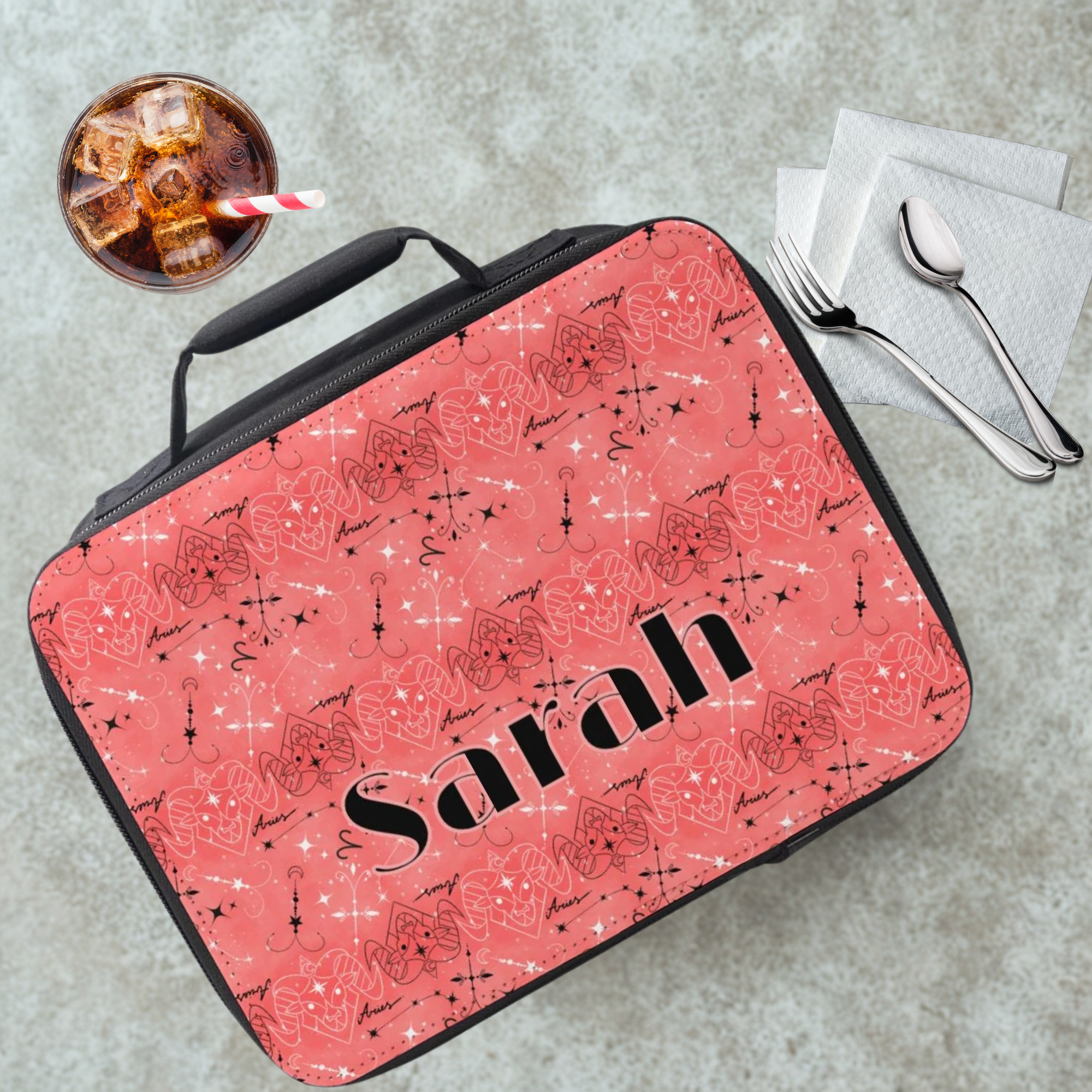  lunch bag with a pink and black Aries zodiac pattern and  'Sarah' custom text, placed on a cafeteria tabe with a drink and utensils