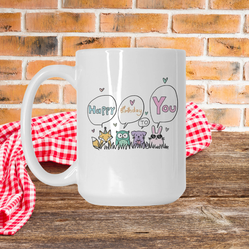 White mug with 'Happy Birthday to You' design on a wooden surface with a red checkered cloth and brick wall background.