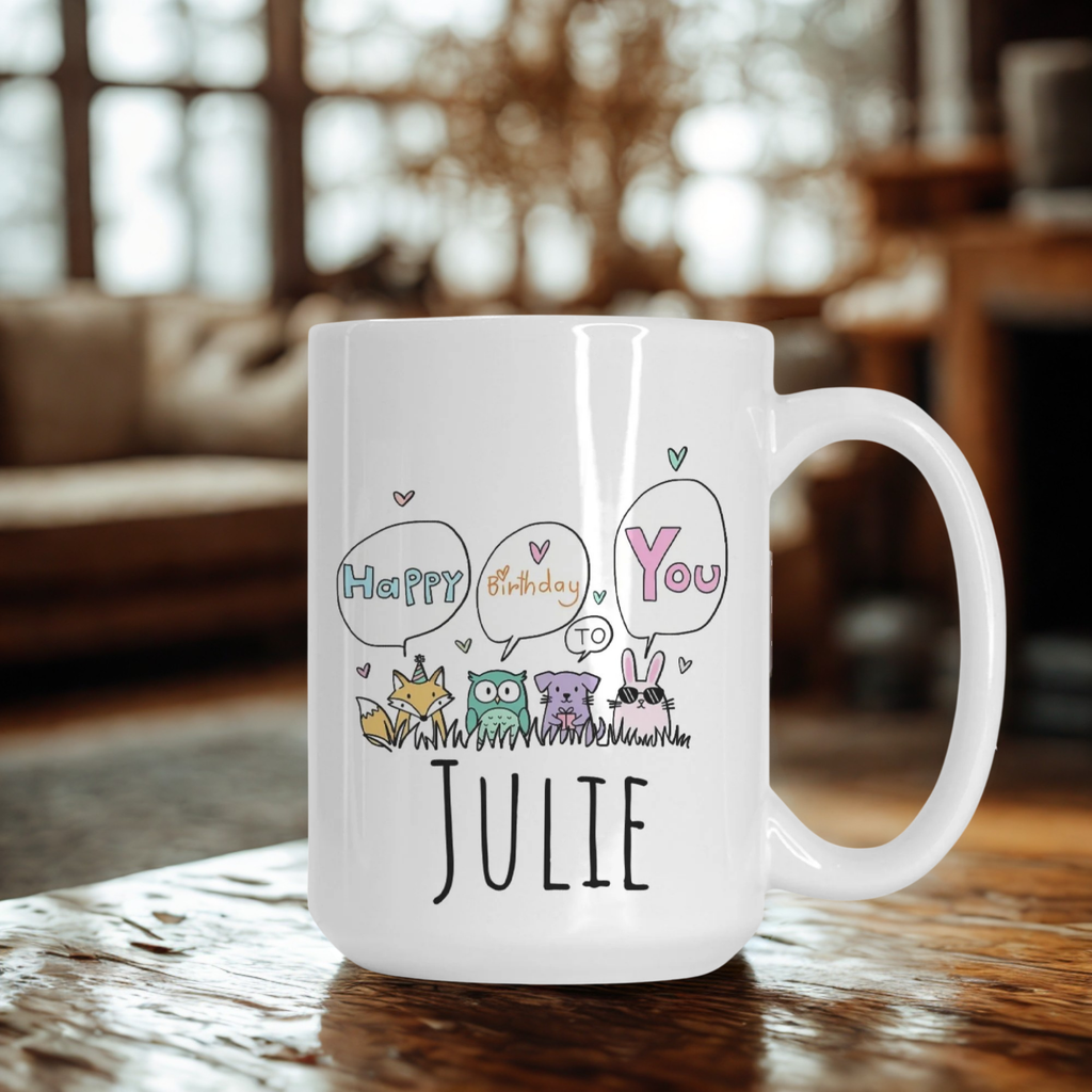 White mug with 'Happy Birthday You Julie' text and cartoon animals on a wooden table.