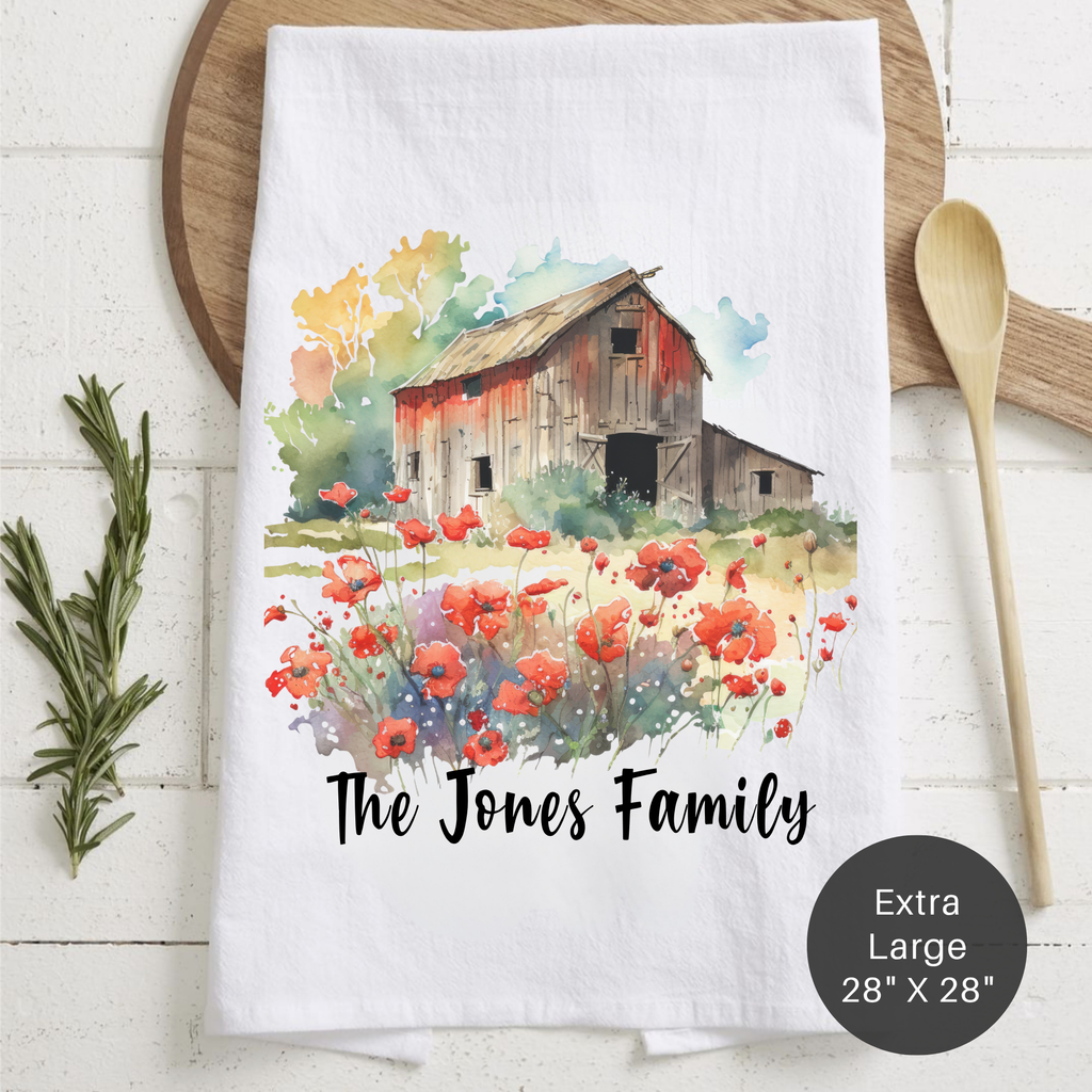 Tea towel with barn and flowers design, featuring 'The Jones Family' text, on a wooden surface.