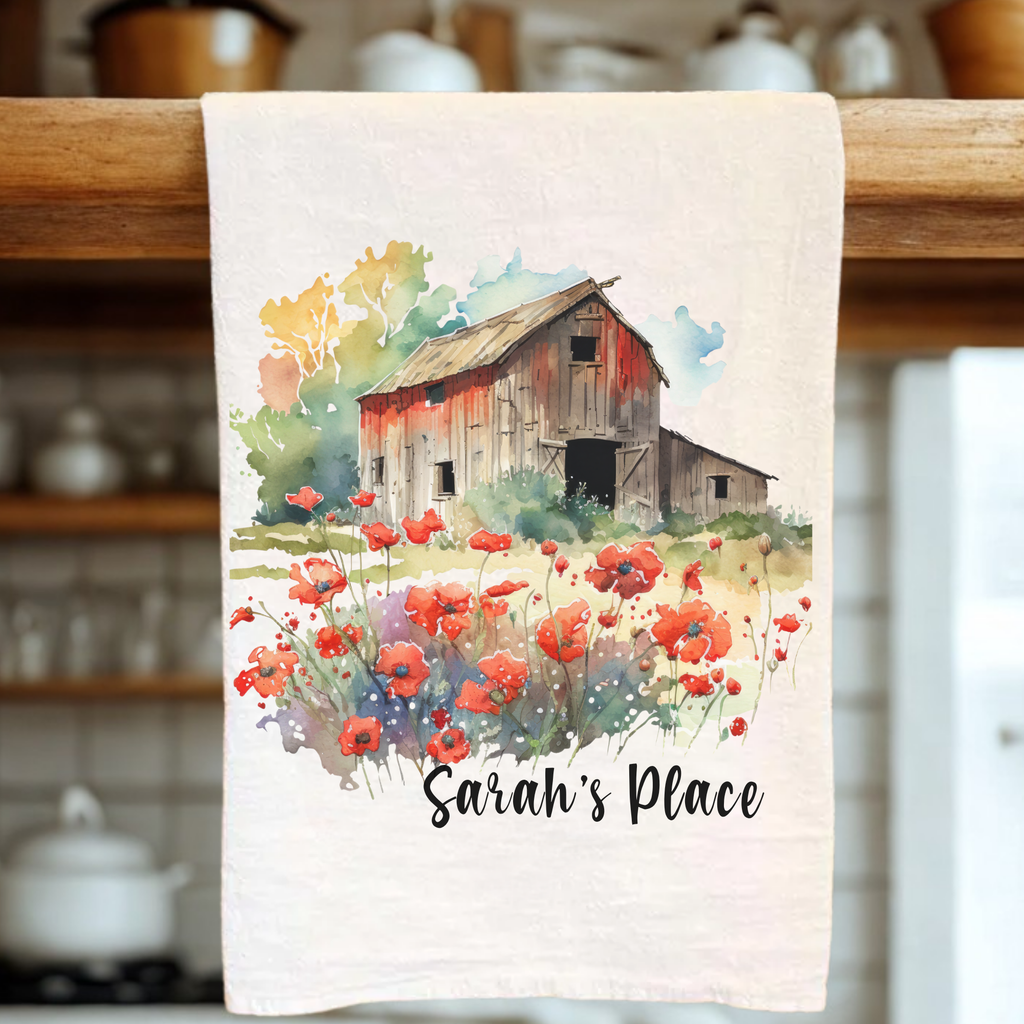 Tea towel with a barn and flower design hanging on a wooden rack in a kitchen.