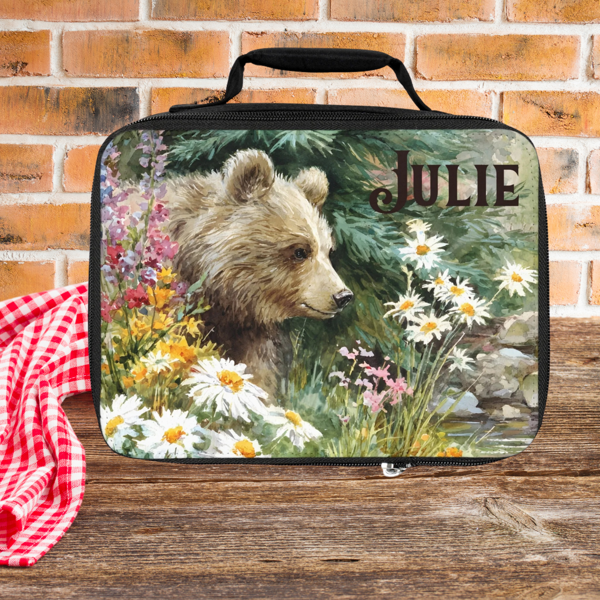  insulated lunch bag with bear design and 'JULIE' personalized text on a wooden picnic table with brick background