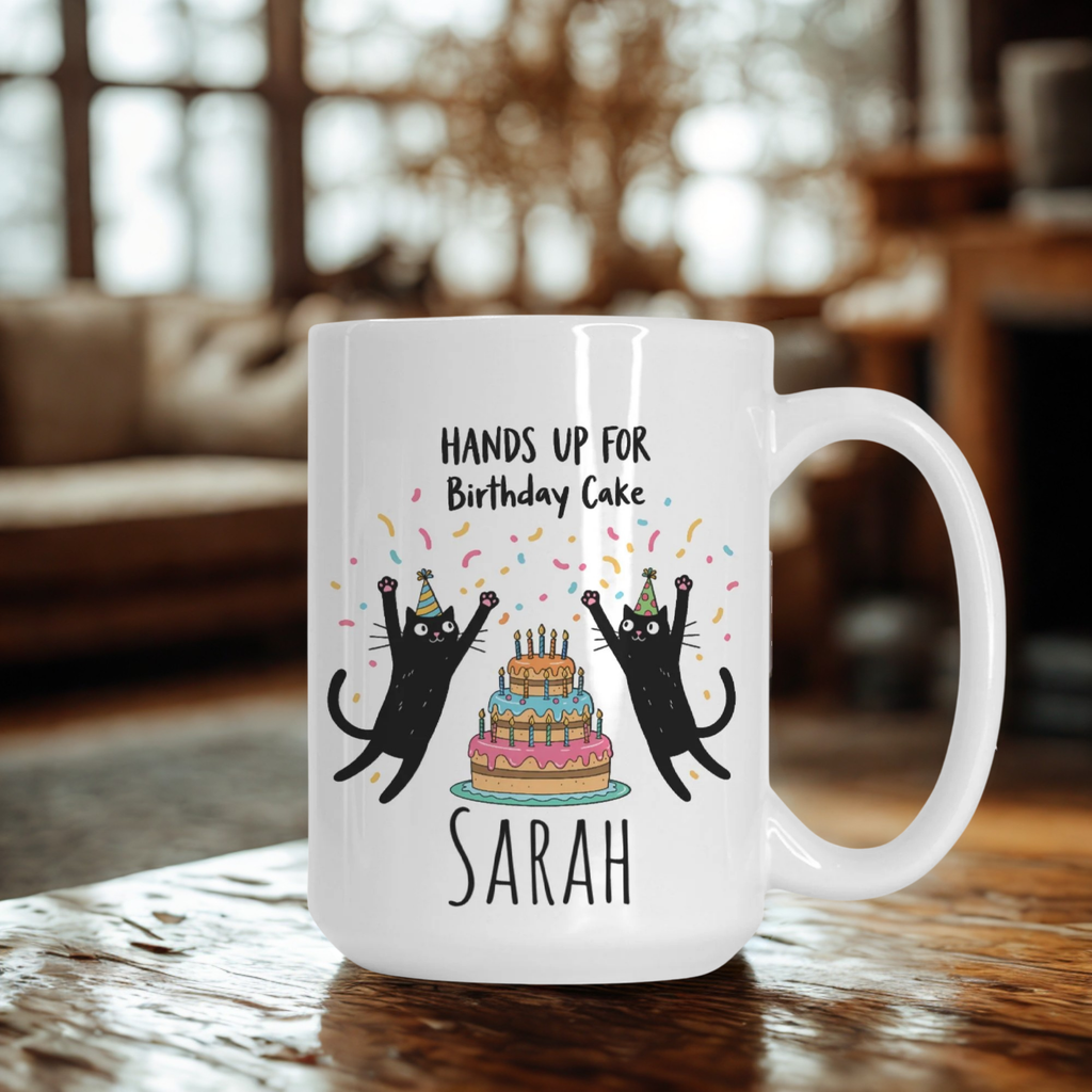 White mug with cartoon cats and birthday cake design on a wooden table.
