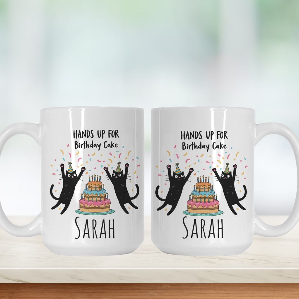 Two white mugs with black cat illustrations and birthday cake design on a white background