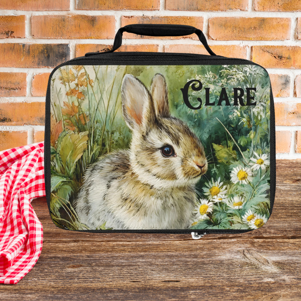 Lunch bag with a rabbit design and 'Clare' text on a picnic table against a brick wall background