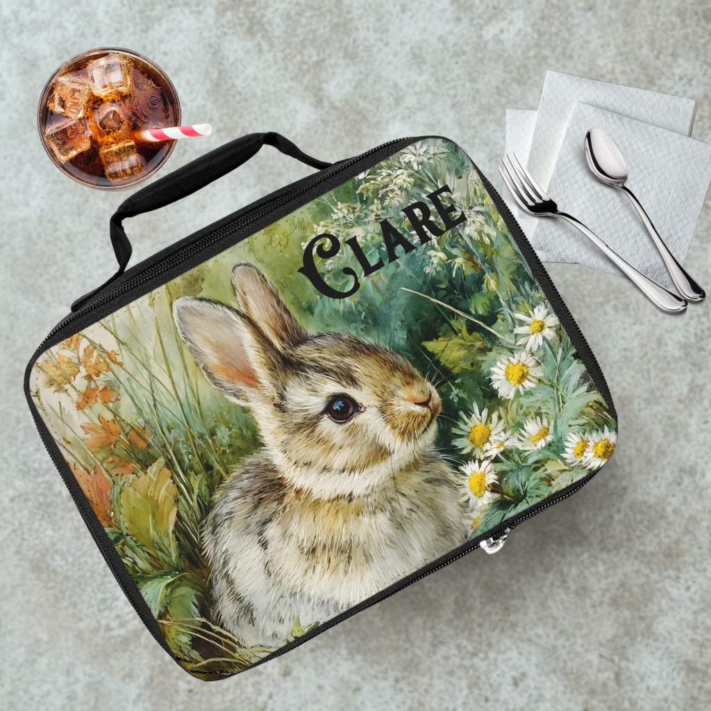 Lunch bag with a rabbit design and 'Clare' text on a table with a drink and utensils.
