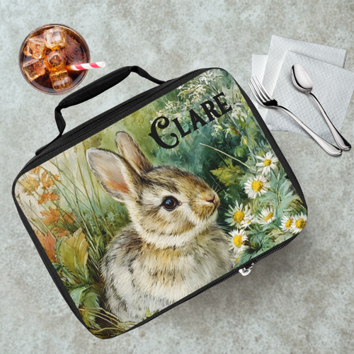 Lunch bag with a rabbit design and 'Clare' text on a table with a drink and utensils.