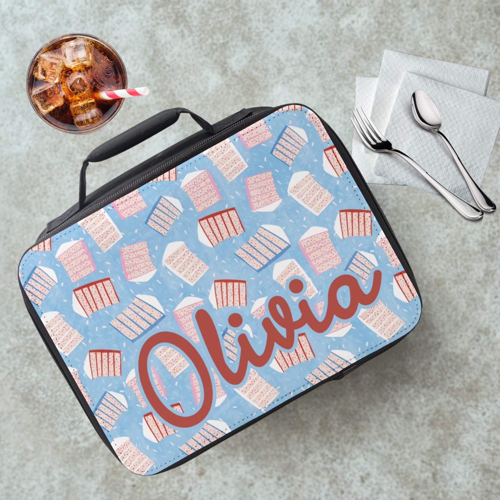 Lunch bag with cake pattern design on a cafeteria table with a drink and utensils.