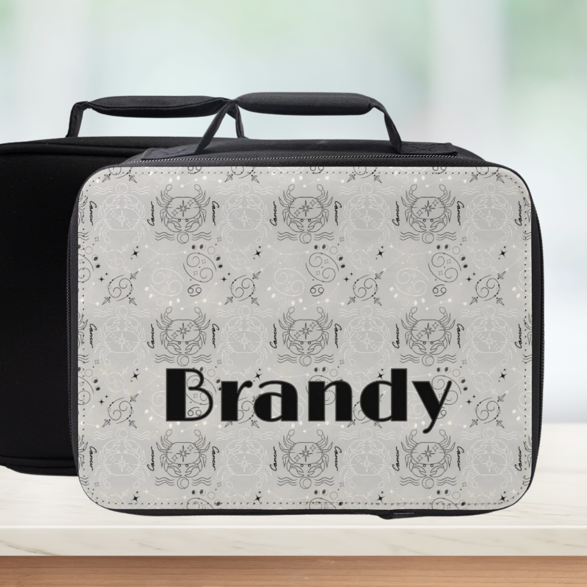 Personalized black and white patterned Cancer zodiac lunch bag with 'Brandy' custom text on a blurred background
