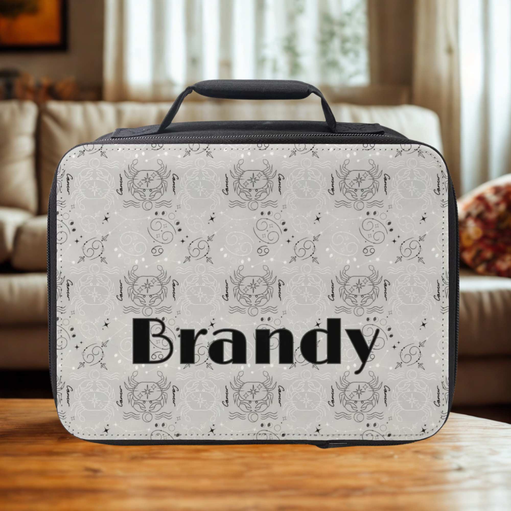 Personalized lunch bag with decorative Cancer zodiac pattern and 'Brandy' custom text on a wooden table in a cozy living room.