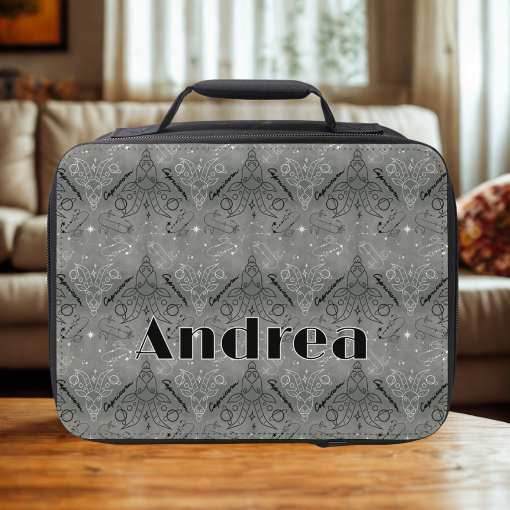 Gray Capricorn zodiac patterned lunch bag with 'Andrea' custom text on a wooden coffee table in a cozy living room.