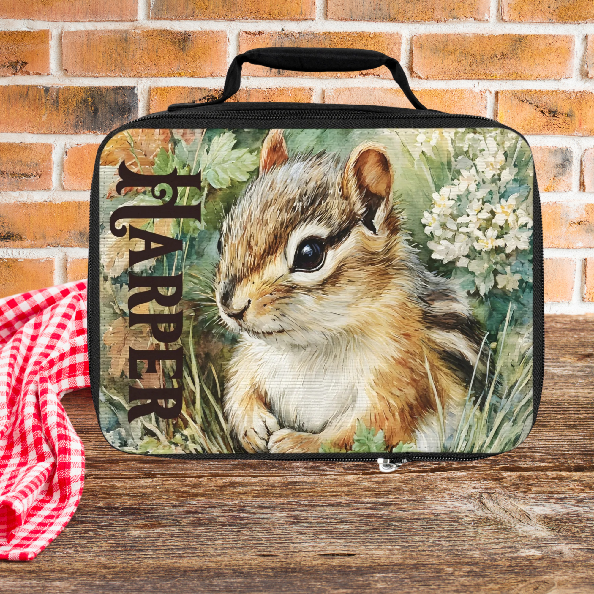 Lunch bag with a chipmunk design and 'Harper' custom text on a wooden picnic table against a brick wall background