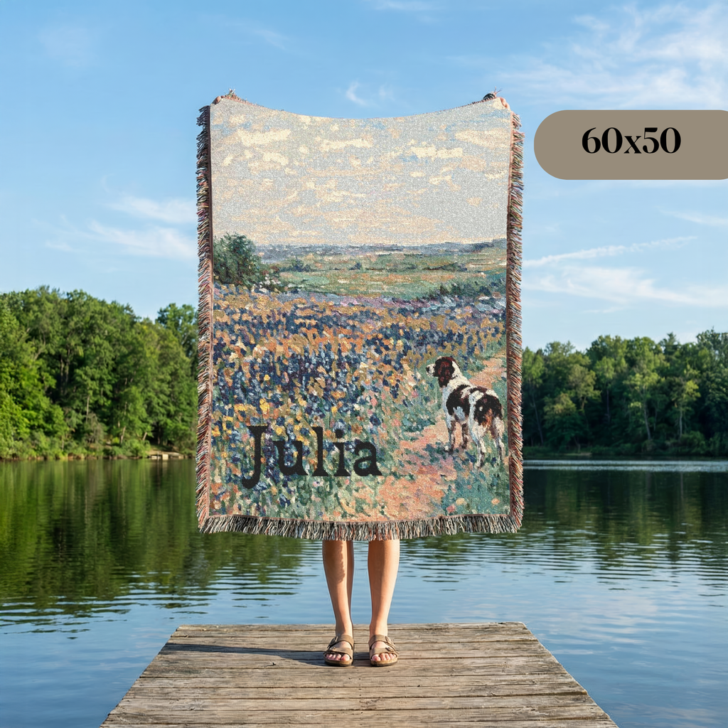 A woven throw blanket with fringe is held up by a person standing on a wooden dock over a lake, showing a landscape print with the name 'Julia' and a dog. A '60x50' size label is visible in the top right.