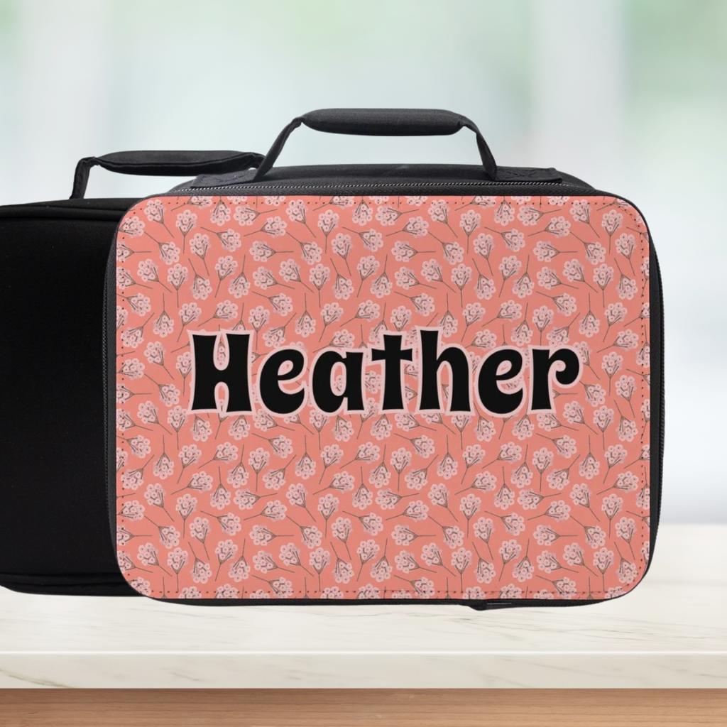 Pink floral patterned suitcase with 'Heather' text on a blurred background