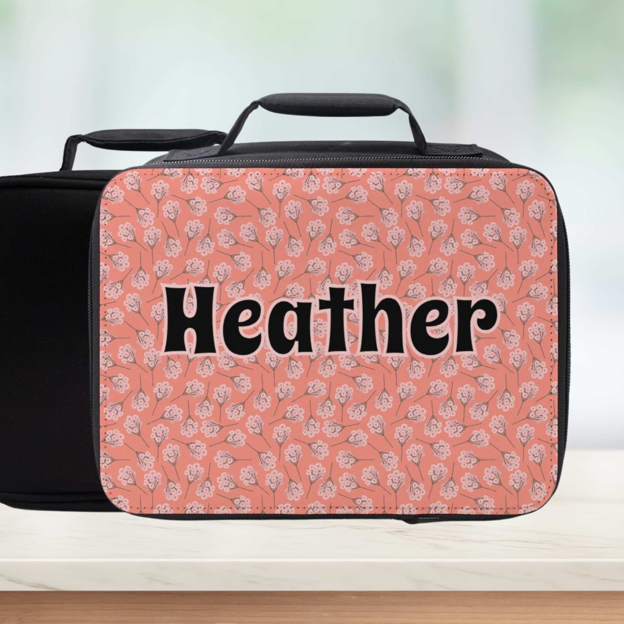 Pink floral patterned suitcase with 'Heather' text on a blurred background
