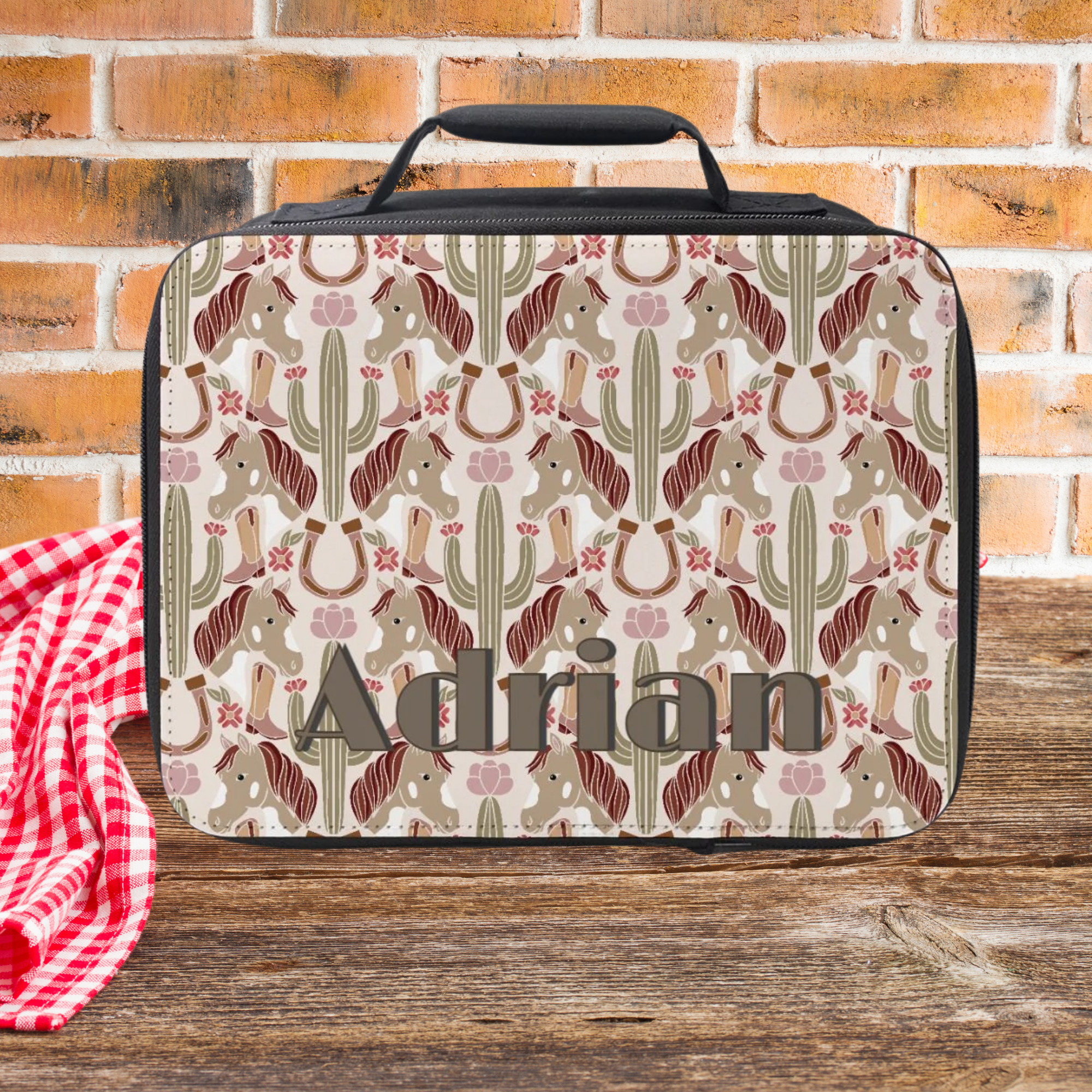 Lunch bag with cowgirl pattern and 'Adrian' custom on a wooden picnic table with brick background