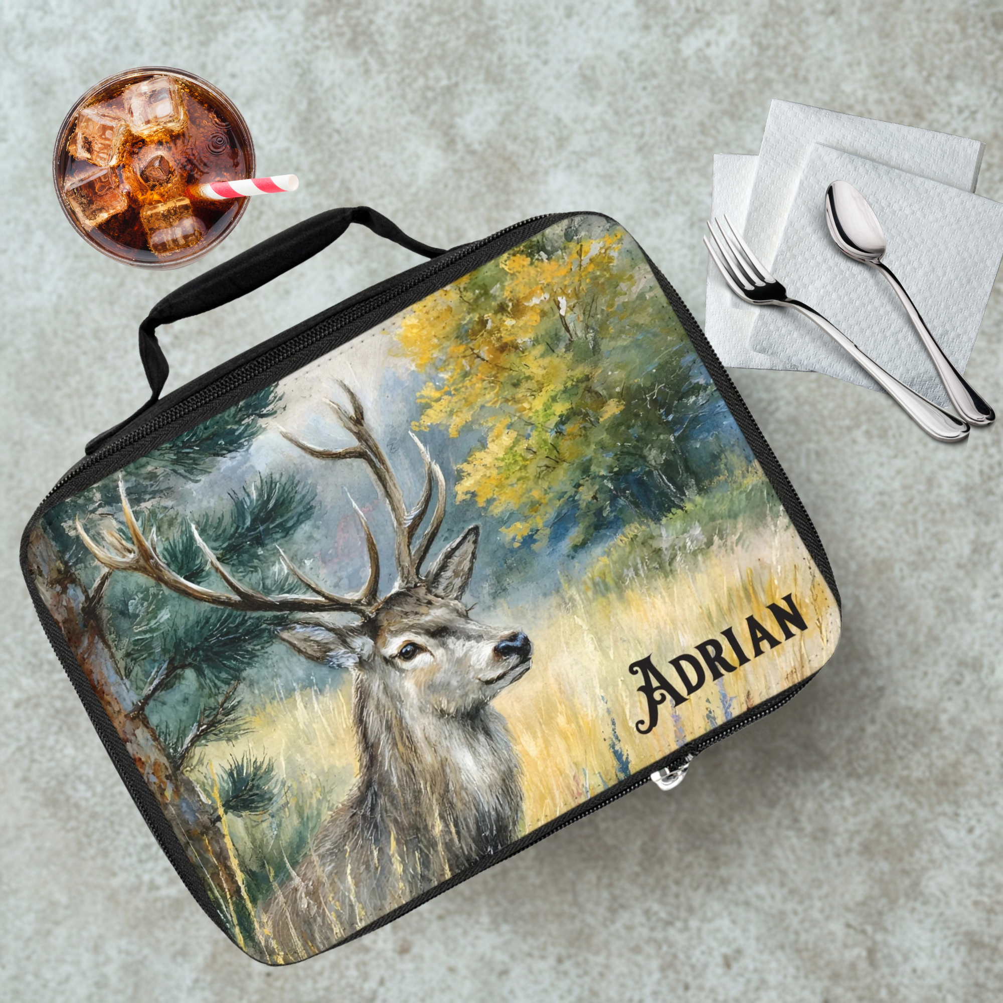  insulated lunch bag with deer design and 'Adrian' personalized text on a cafeteria table with a drink and utensils.