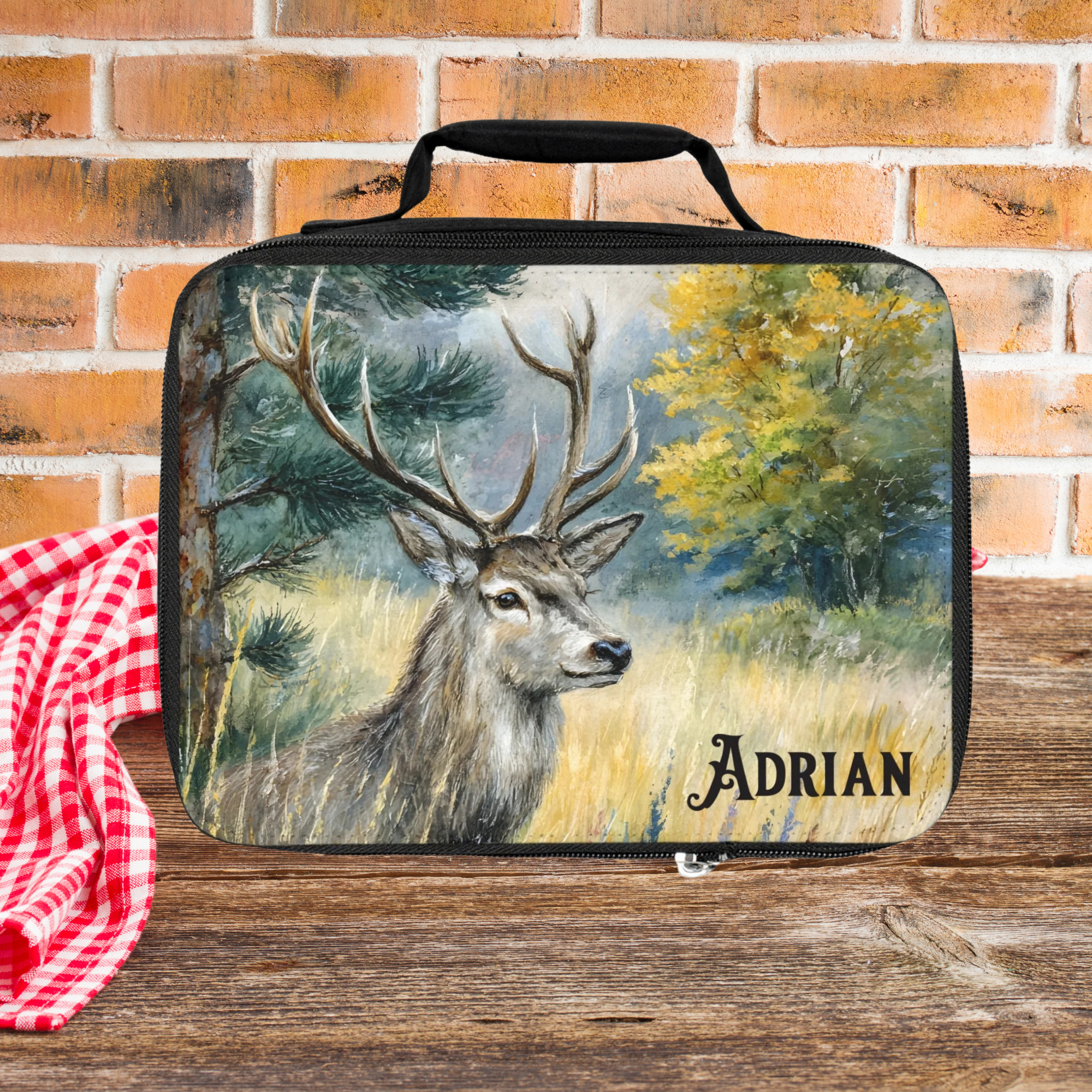 Lunch bag with deer design and 'Adrian' personalized text on a picnic table against a brick wall background