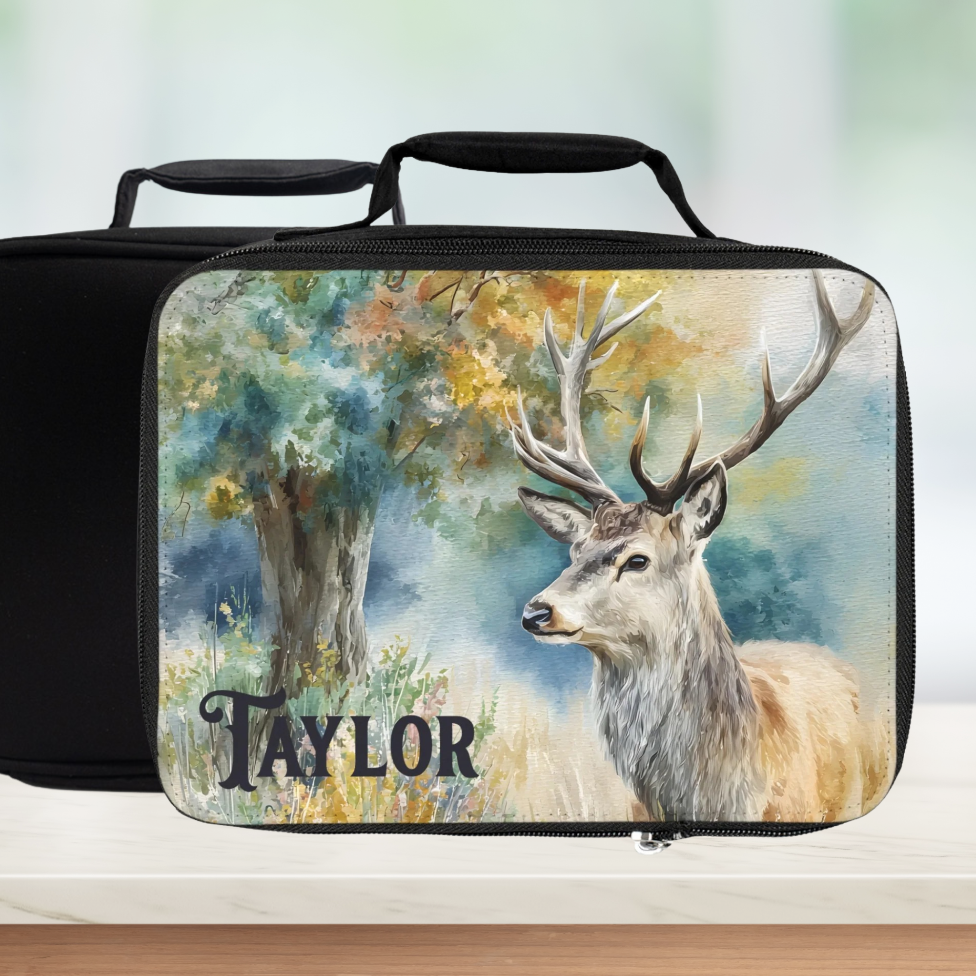 Black lunch bag with a deer design and 'Taylor' text on a blurred nature background