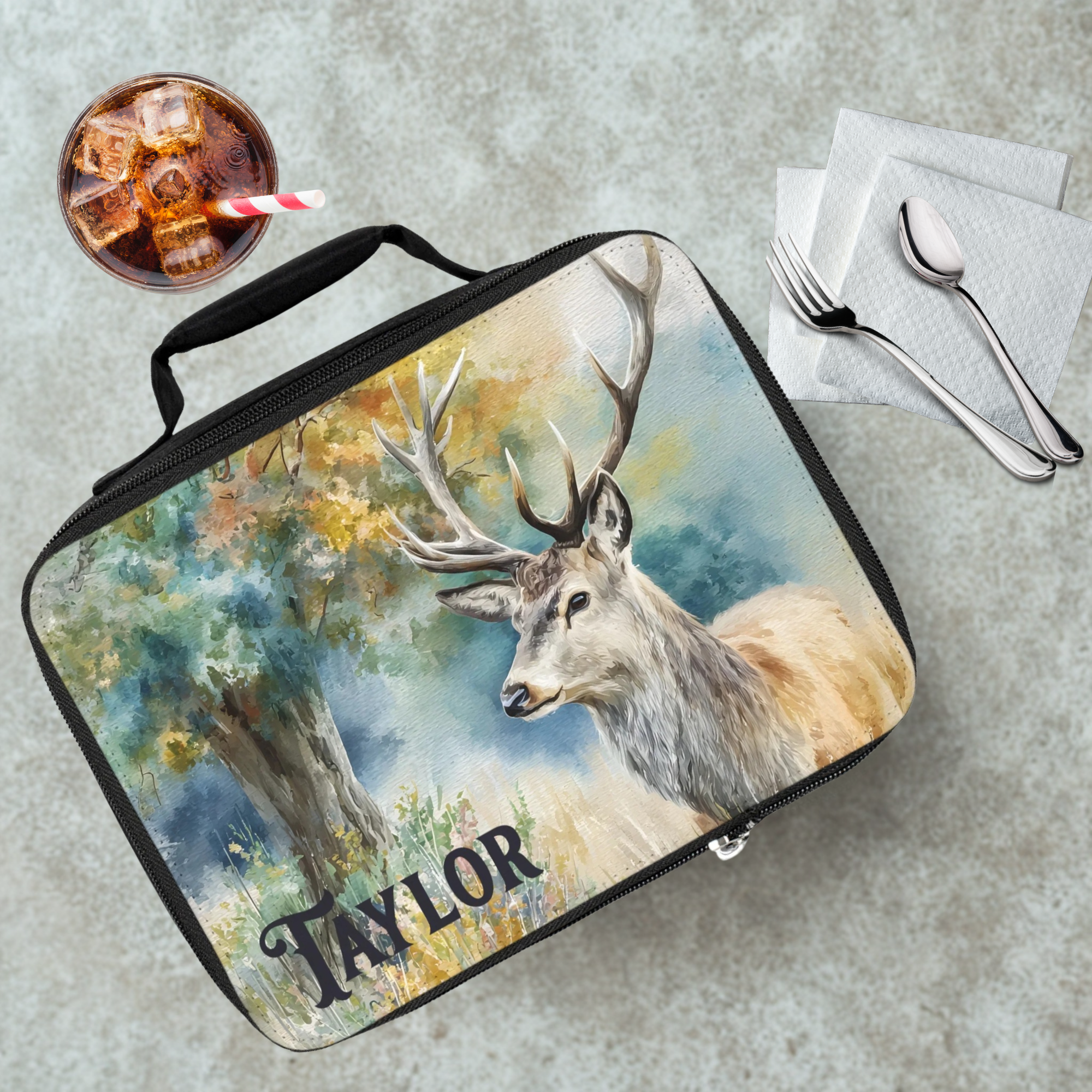  insulated lunch bag with deer design and 'Taylor' text on a cafeteria table with a drink and eating utensils.