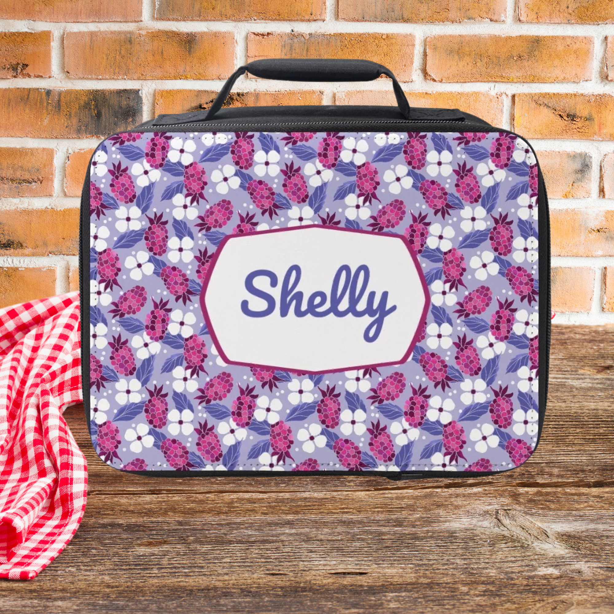 Floral patterned lunch bag with 'Shelly' on a wooden picnic table and brick wall background