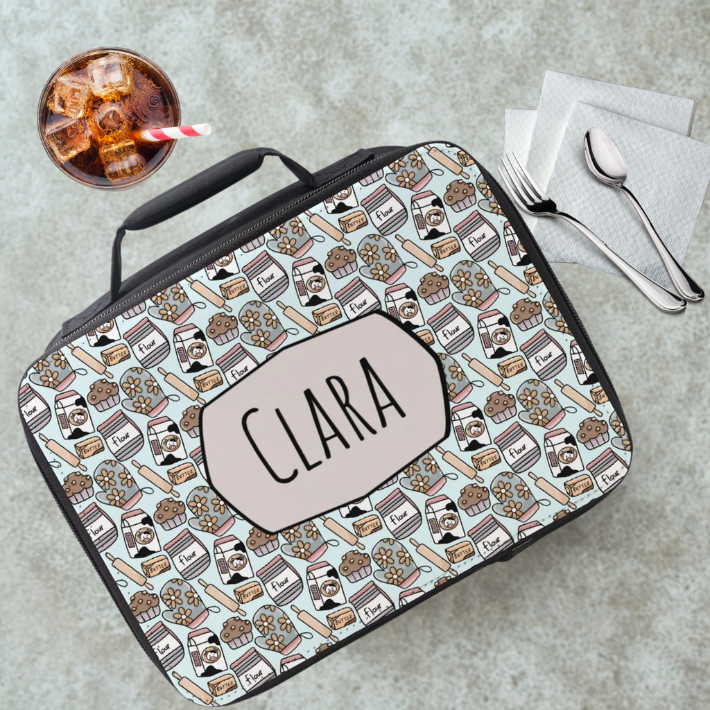 Lunch bag with 'CLARA' custom name and food pattern on a cafeteria table with a drink and utensils.
