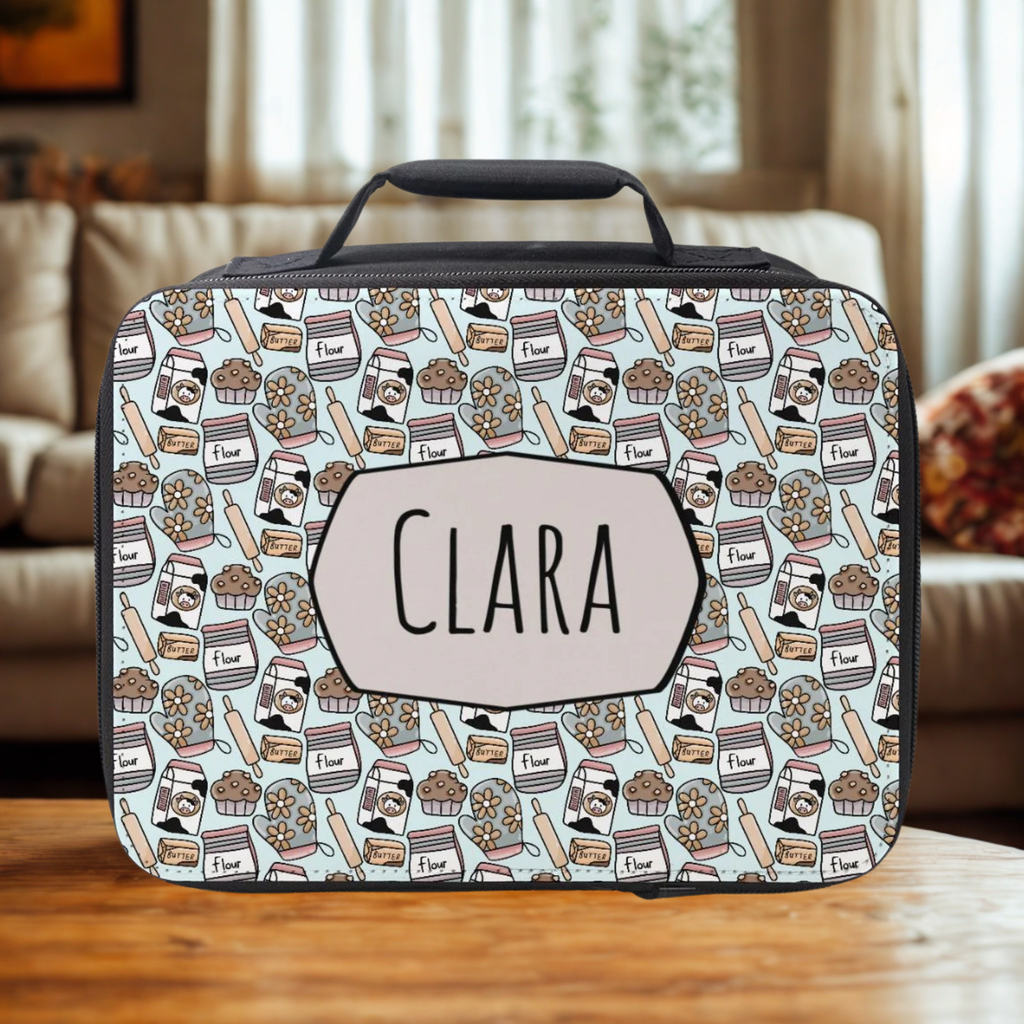  insulated lunch bag with baking-themed pattern and 'Clara' personalized name on a wooden living room table