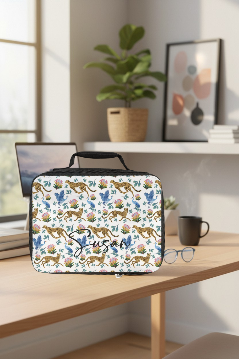 Insulated lunch bag with a cheetah pattern design on a desk with a laptop, mug, and glasses.